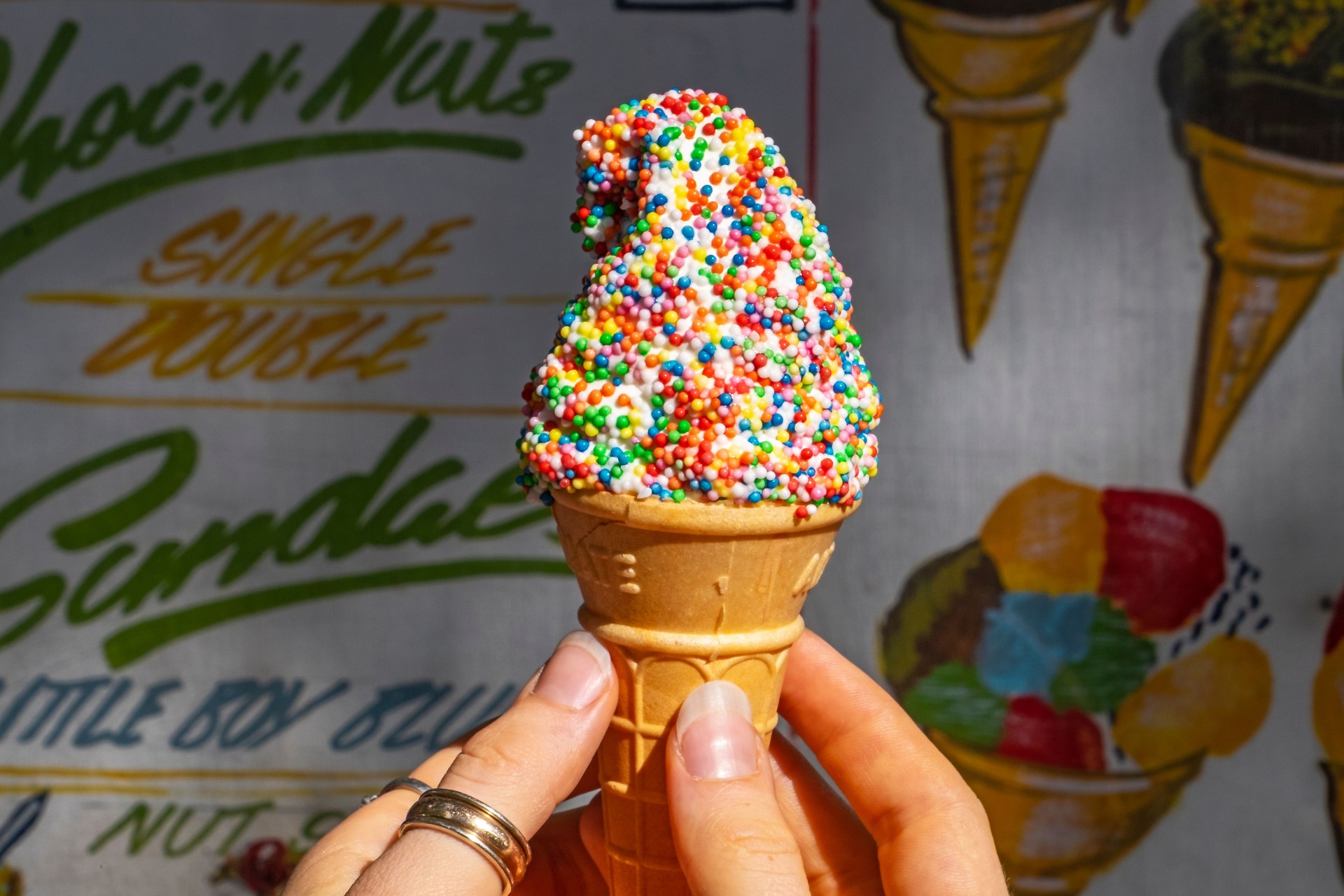 Female hands receiving a soft serve ice cream cone with sugar sprinkles or sparkles